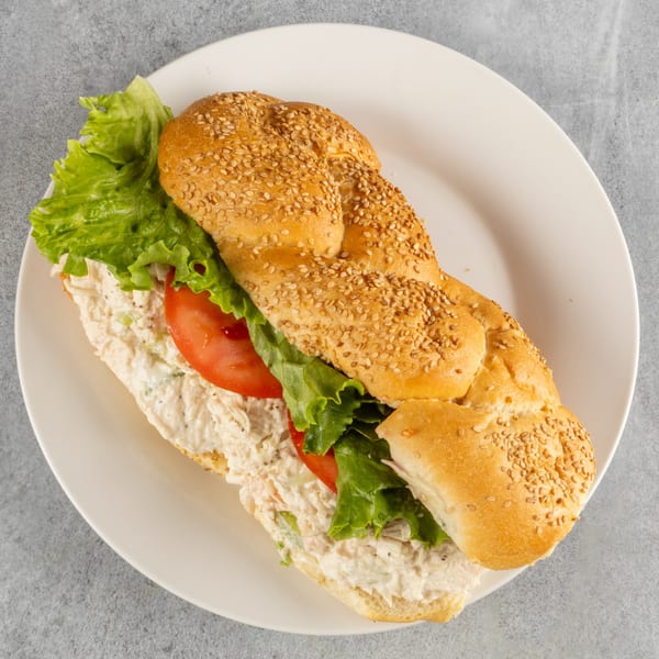 A chicken salad sub sandwich with lettuce and tomato on a sesame seed braided roll.