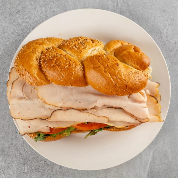 Top-down view of a turkey sandwich on braided bread with lettuce and tomato on a white plate.