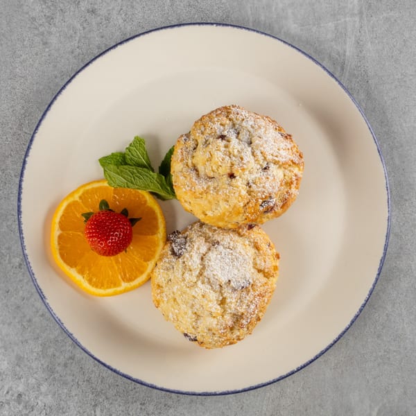 Two powdered sugar scones with an orange slice, strawberry, and mint on a white plate.