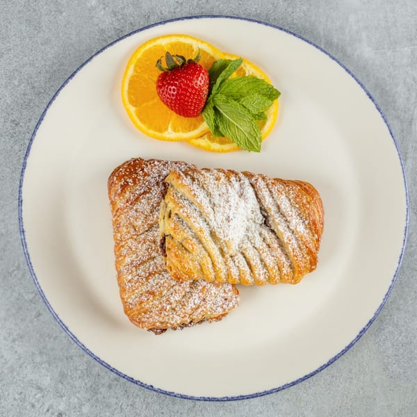 Two powdered sugar pastries with orange slices, a strawberry, and mint on a white plate.