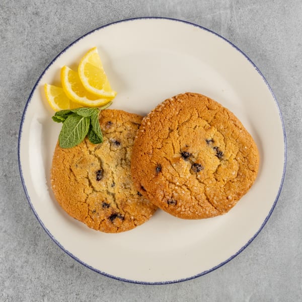 Two blueberry cookies with lemon slices and mint on a white plate.