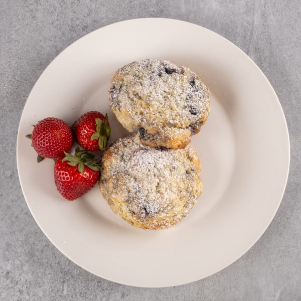 Two powdered sugar muffins with three fresh strawberries on a white plate.