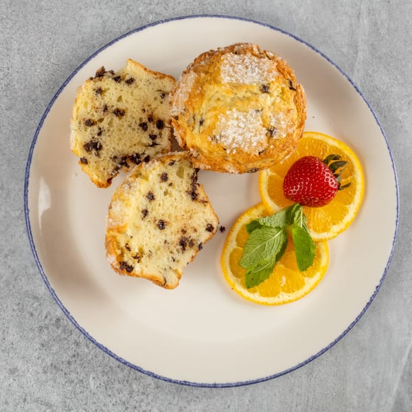 Chocolate chip muffin, one whole and one cut in half, with orange slices, strawberry, and mint.
