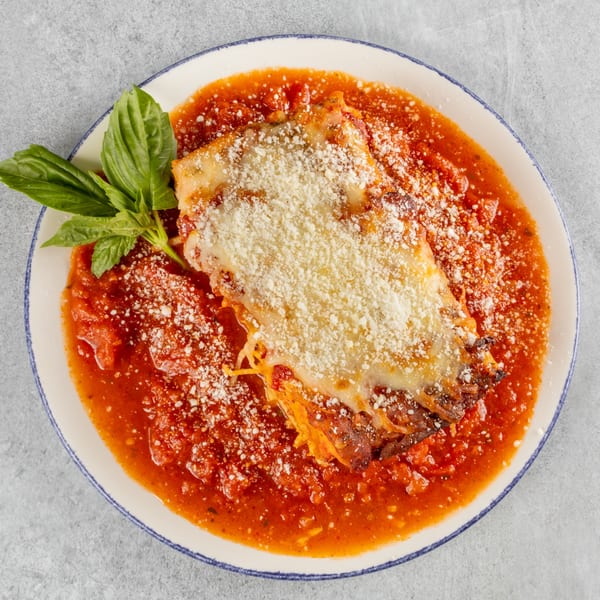 A serving of lasagna with melted cheese and tomato sauce, garnished with fresh basil leaves.