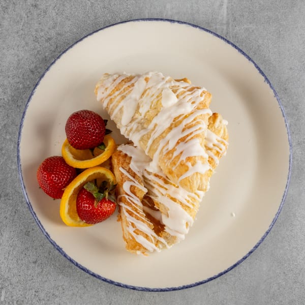 Two glazed croissants with strawberries and orange slices on a white plate.