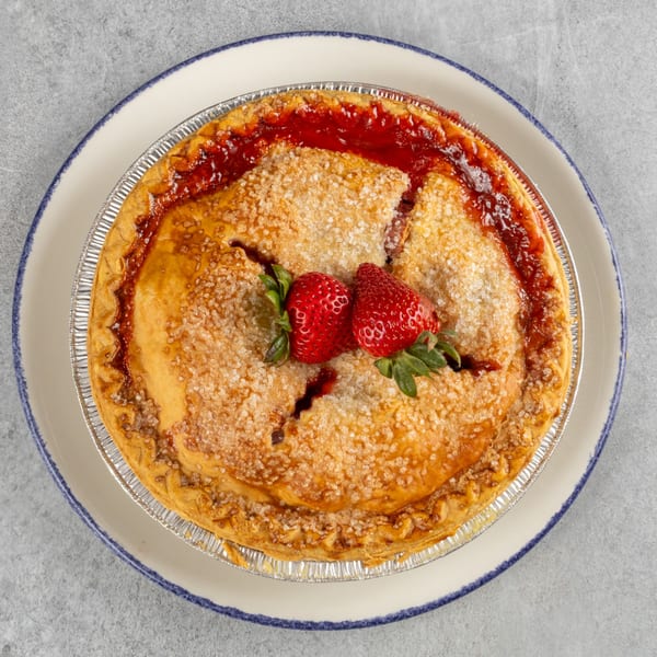 A freshly baked strawberry pie in a foil tin, garnished with two whole strawberries on a white plate.