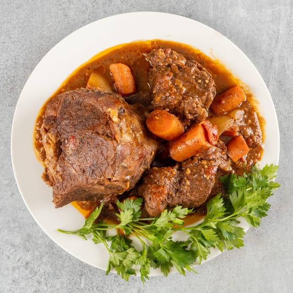 Hearty beef stew with carrots and potatoes, garnished with fresh parsley on a white plate.
