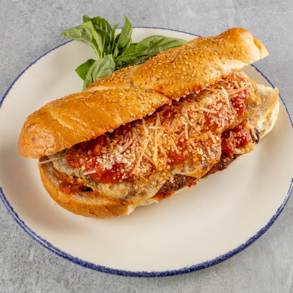 Eggplant parmesan hero sandwich with marinara sauce, melted cheese, and basil on a white plate.