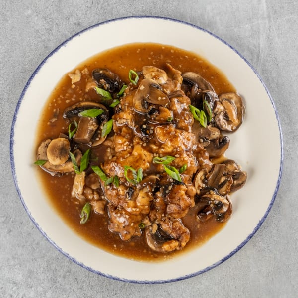 Chicken and mushrooms in a rich brown sauce, garnished with green onions on a white plate.