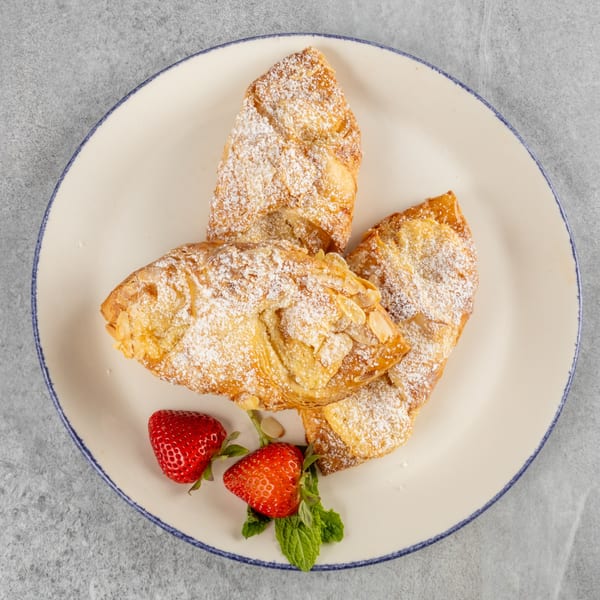 Three almond croissants dusted with powdered sugar, garnished with strawberries and mint on a white plate.