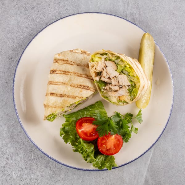 Grilled chicken Caesar wrap, cut in half, with a pickle spear, lettuce, tomatoes, and parsley.