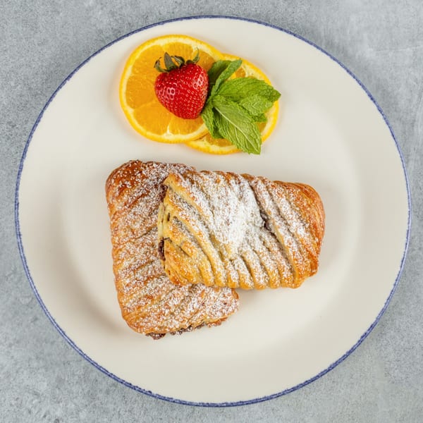 Two pastries dusted with powdered sugar, garnished with orange slices, a strawberry, and mint.