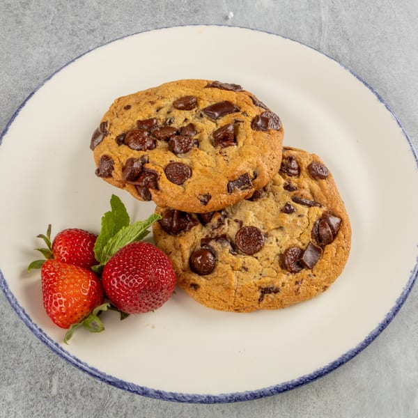 Two chocolate chip cookies with fresh strawberries and mint on a white plate.