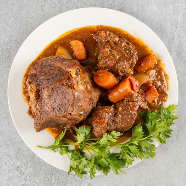 Hearty beef stew with carrots and parsley in a rich brown sauce on a white plate.