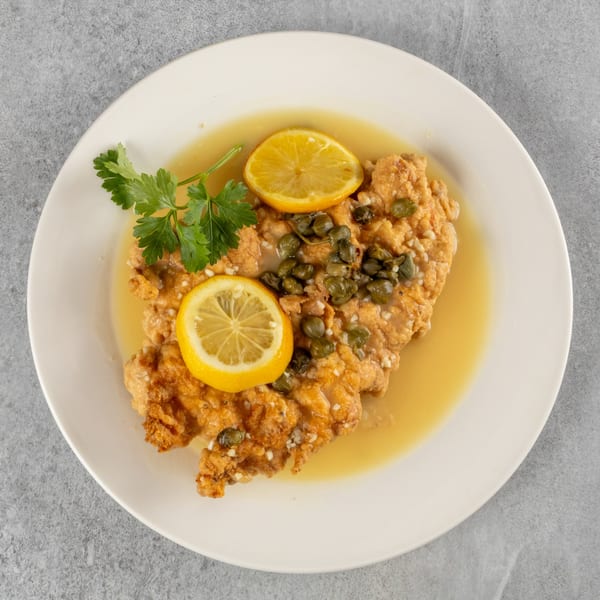 Fried chicken cutlet in a lemon-caper sauce, garnished with parsley and lemon slices.